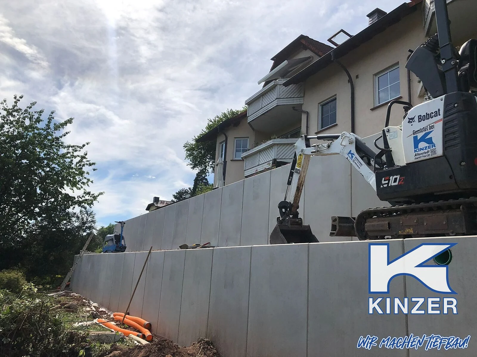 Winkelstützelemente aus Beton an einem Hang vor einem Mehrfamilienhaus, Bild mit Kinzer-Wasserzeichen