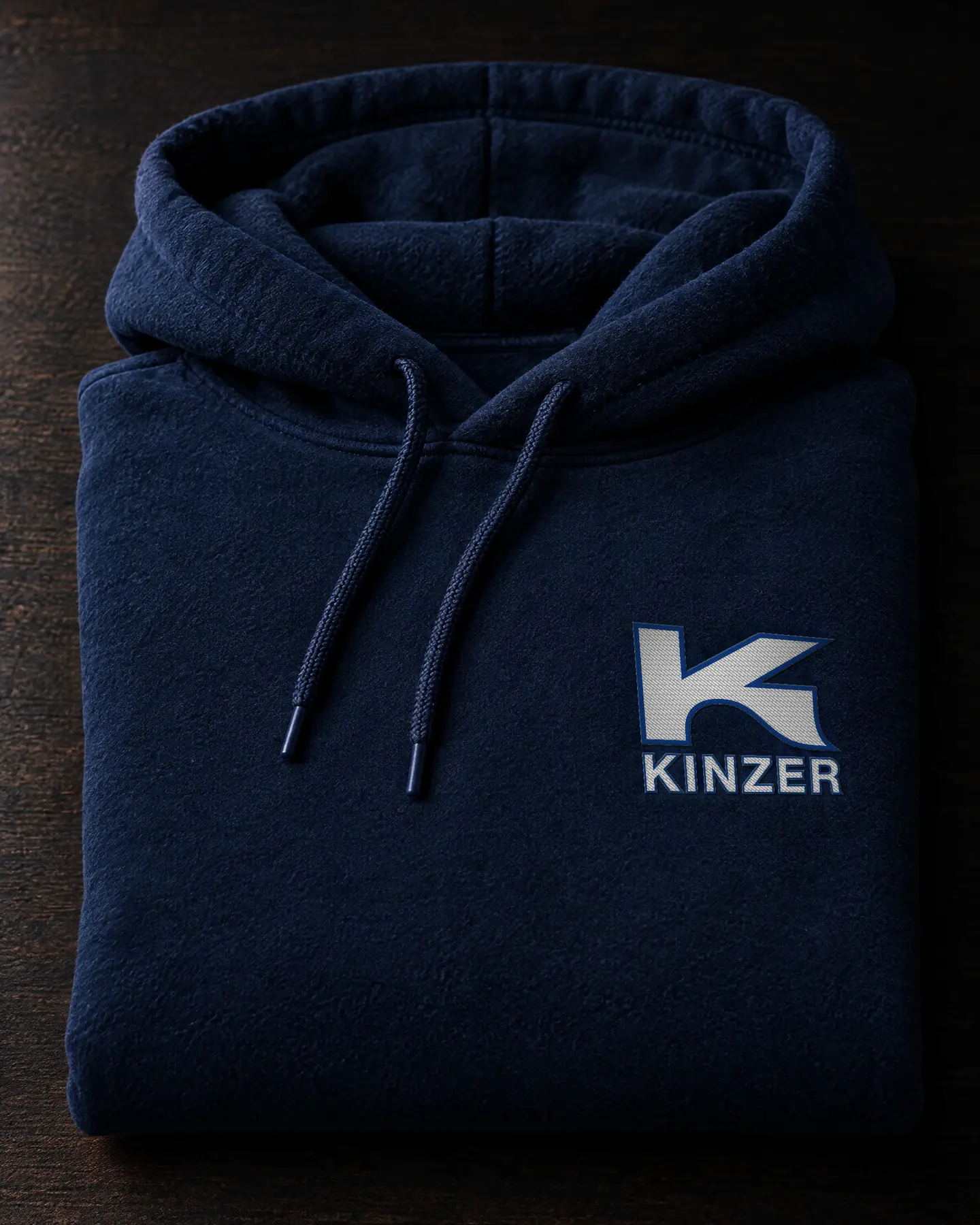 Gefalteter dunkelblauer Hoodie mit gesticktem Kinzer-Logo auf der Brust